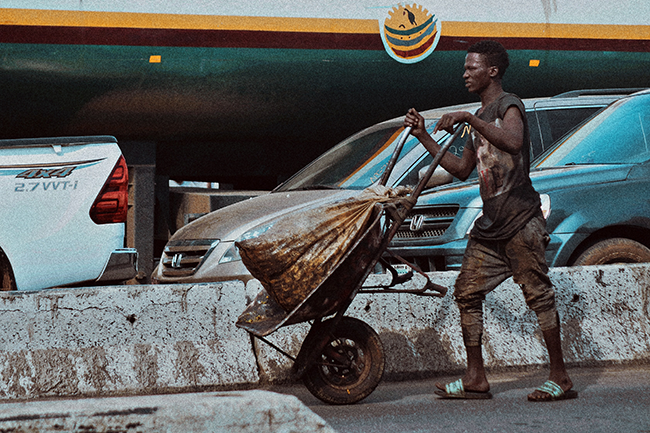 A Porter, also known as Alabarau, rolls a wheel barrow in a Lagos Market as a means of survival. Credit: Shedrack Salami via Unsplash