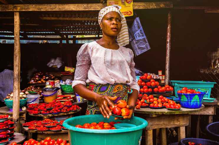 A woman stands in front of her vegetable stall. Credit: Canva