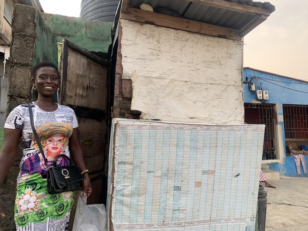 Iya Ibeji Lotto stands next to her kiosk in Kokumo.